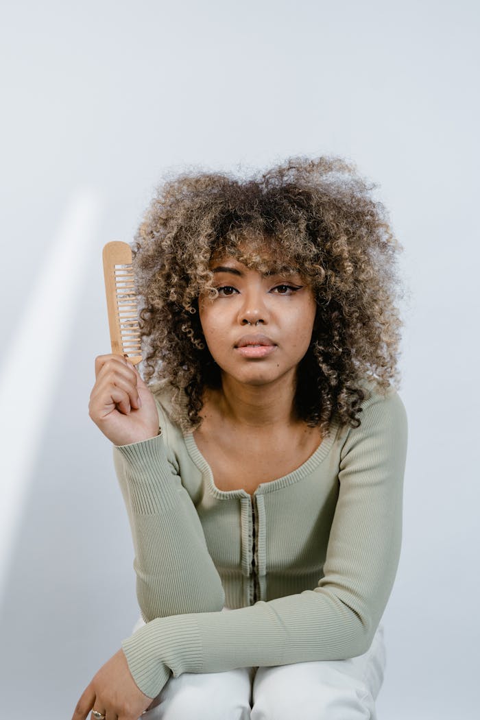 gallery-03 Portrait of a woman with natural afro hair holding a wooden comb, emphasizing beauty routines.